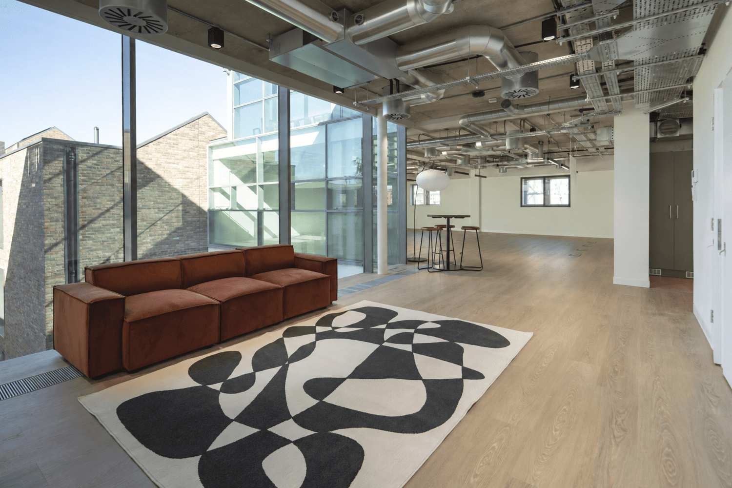 Light-filled breakout space at Primrose Hill Works, with comfortable lounge seating, floor-to-ceiling windows and views across the canal-side workspace.