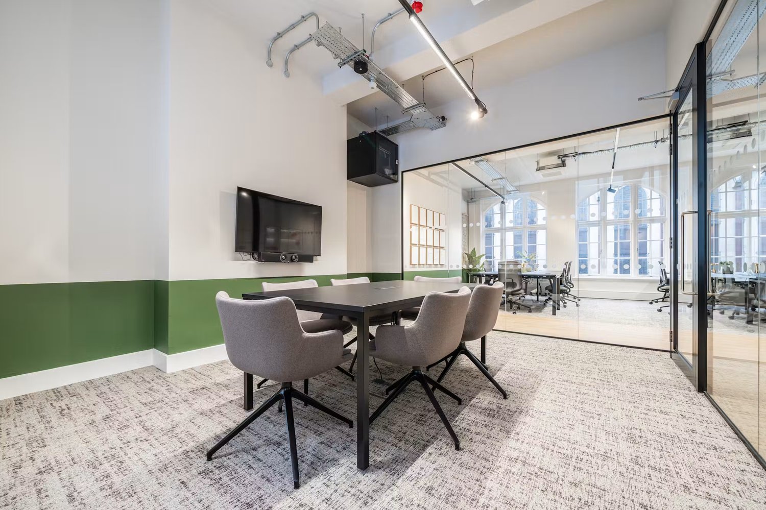 A dedicated meeting room with upholstered seating and a wall-mounted screen provides space for focused discussions and presentations.