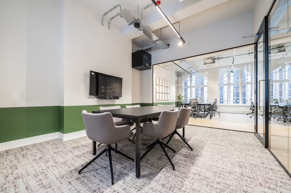 A dedicated meeting room with upholstered seating and a wall-mounted screen provides space for focused discussions and presentations.
